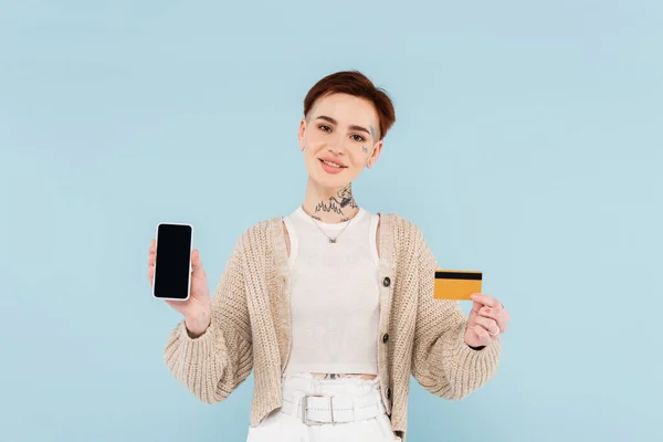 Mujer alegre sosteniendo tarjeta de crédito y teléfono inteligente con pantalla en blanco aislado en azul - foto de stock