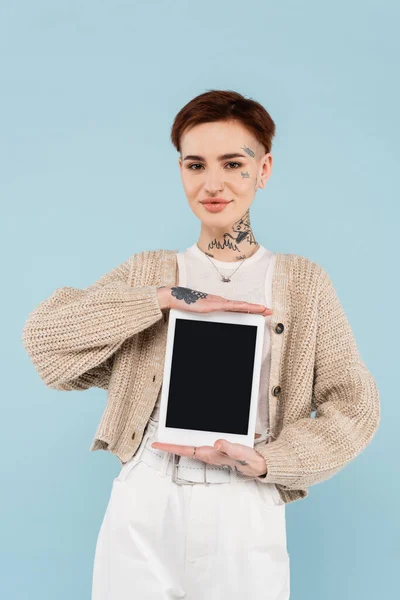 Щаслива молода жінка з татуюваннями тримає цифровий планшет з порожнім екраном ізольовано на синьому — стокове фото