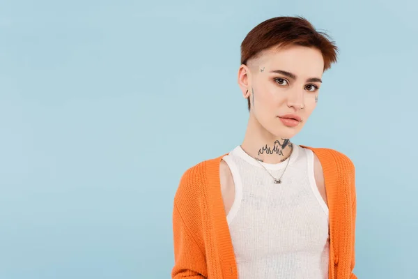 Young woman with tattoos in orange cardigan looking at camera isolated on blue — Stock Photo