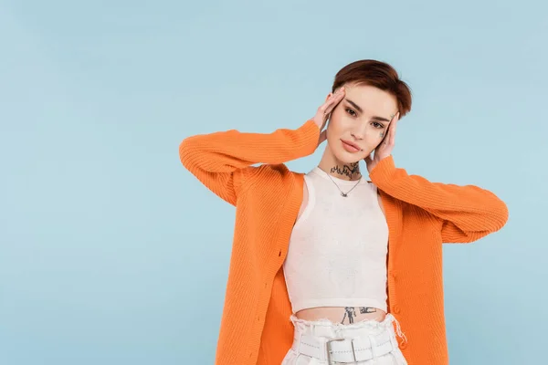 Pretty young woman with tattoos in orange cardigan posing isolated on blue — Stock Photo
