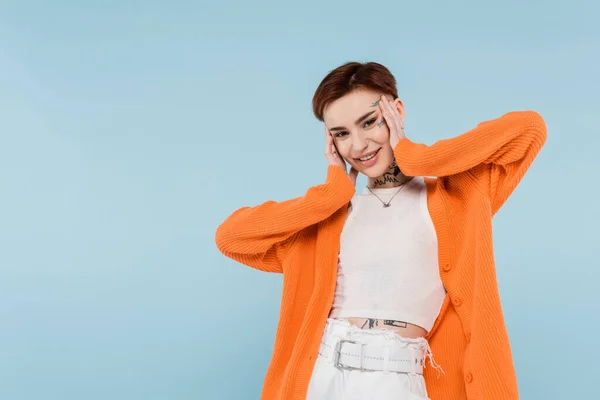 Heureuse jeune femme avec des tatouages en cardigan orange posant isolé sur bleu — Photo de stock