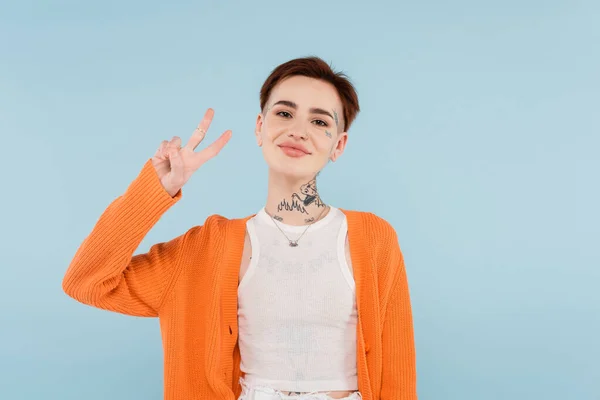 Happy young woman with tattoos showing peace sign isolated on blue — Stock Photo