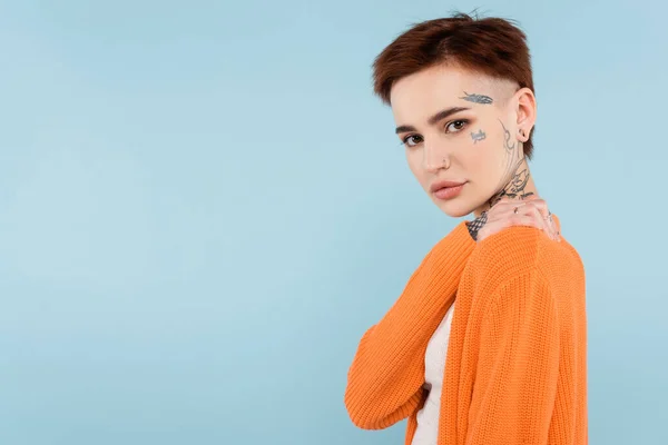 Jeune femme tatouée en cardigan orange posant isolée sur bleu — Stock Photo