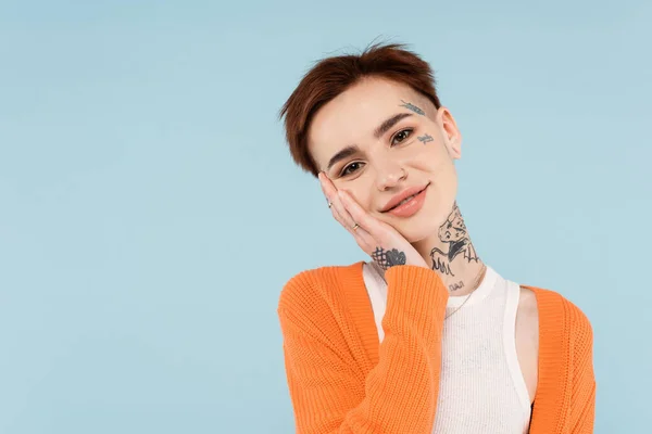 Happy young tattooed woman in orange cardigan posing isolated on blue — Stock Photo