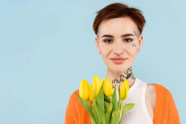 Allegra donna tatuata in cardigan arancione con tulipani gialli isolati su blu — Foto stock