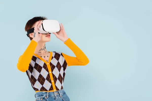 Young tattooed woman adjusting vr headset isolated on blue — Stock Photo