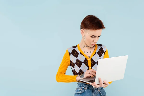 Young and tattooed student using laptop isolated on blue — Stock Photo