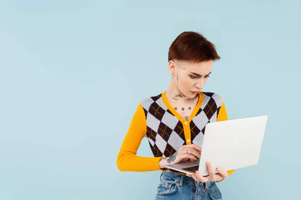 Estudiante joven y tatuado utilizando el ordenador portátil aislado en azul — Stock Photo