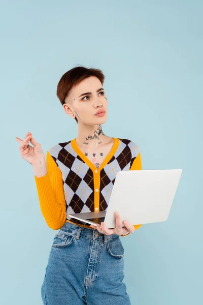 Pensive and tattooed student using laptop isolated on blue — Stock Photo