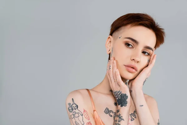 Jeune femme tatouée toucher visage isolé sur gris — Photo de stock