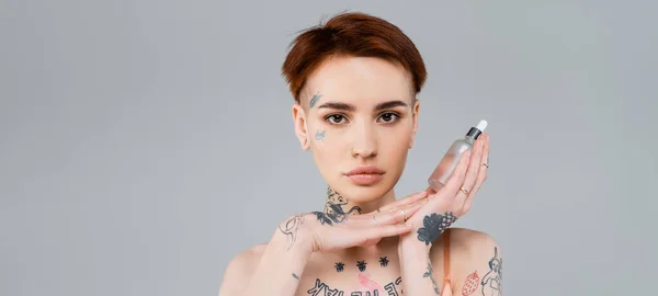 Tattooed young woman holding bottle with serum isolated on grey, banner — Stock Photo