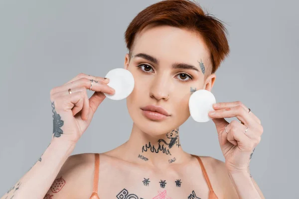 Jeune femme tatouée tenant des tampons de coton isolés sur gris — Photo de stock