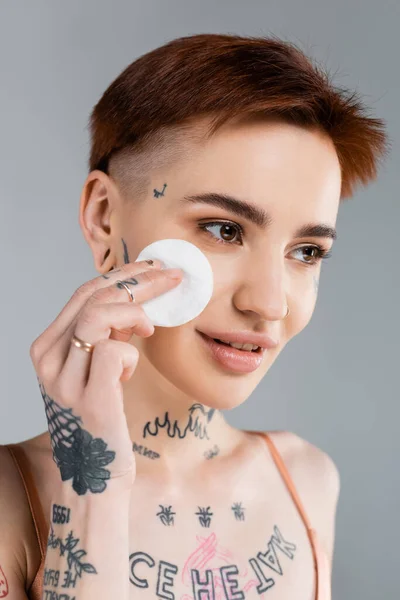 Mujer feliz y tatuada sosteniendo almohadilla de algodón aislado en gris - foto de stock