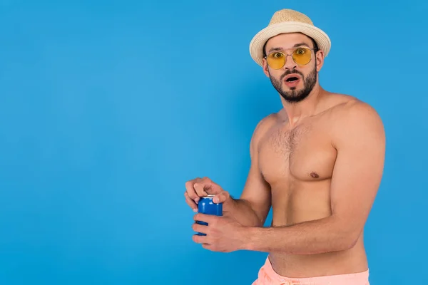Захоплений без сорочки чоловік у солом'яному капелюсі та сонцезахисних окулярах тримає консервований напій ізольовано на синьому — стокове фото