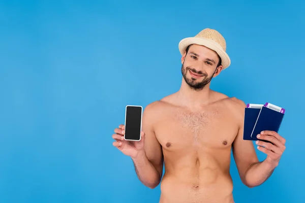 Homem sem camisa em chapéu de sol segurando smartphone e passaportes isolados em azul — Fotografia de Stock