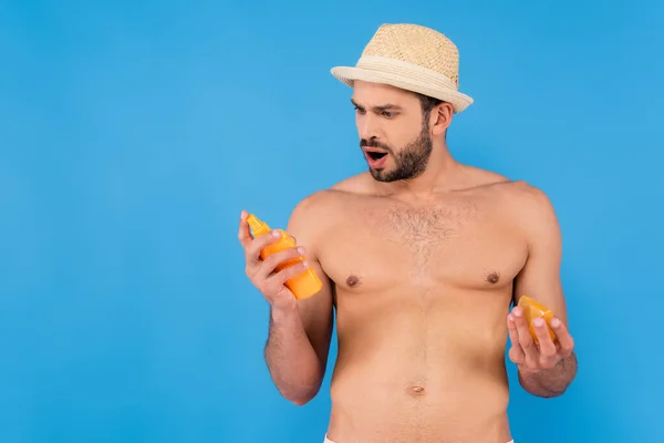 Homme étonné en chapeau de soleil tenant la crème solaire isolée sur bleu — Photo de stock