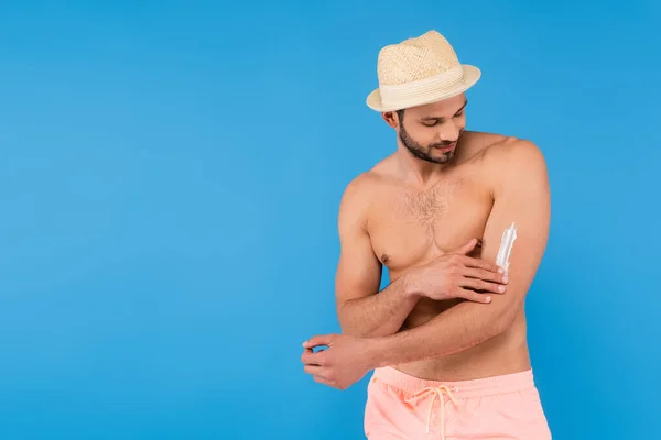 Uomo barbuto con cappello di paglia che applica protezione solare isolata su blu — Stock Photo