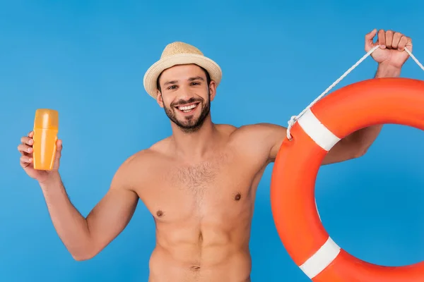 Homem sorridente segurando bóia da vida e protetor solar isolado em azul — Fotografia de Stock