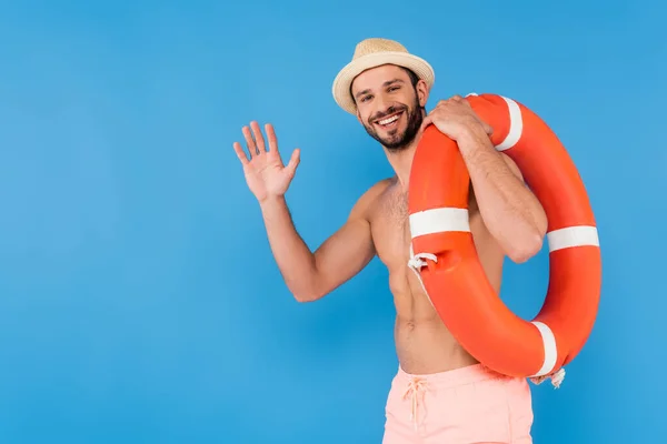 Позитивный человек в солнечной шляпе размахивая рукой и держа спасательный буй изолирован на голубом — стоковое фото
