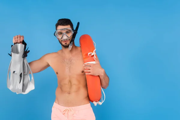 Shirtless man in swimming goggles holding life buoy and flippers isolated on blue — Stock Photo