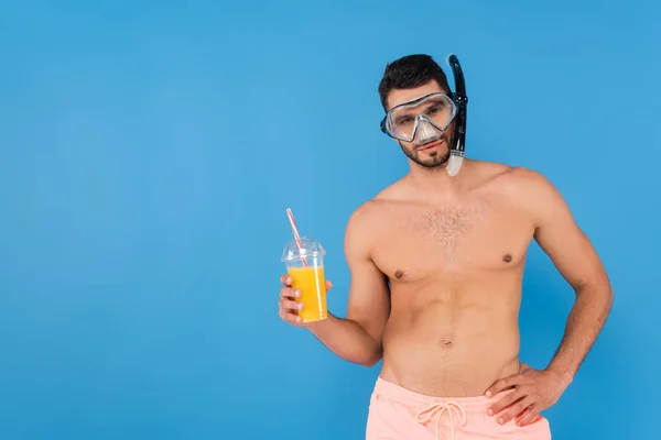 Hombre sin camisa en gafas de natación sosteniendo jugo de naranja aislado en azul - foto de stock