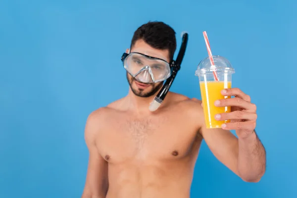 Orange juice in hand of blurred man in swimming goggles isolated on blue — Stock Photo