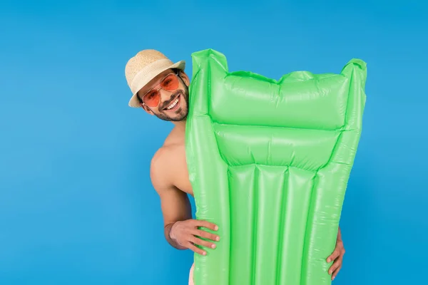 Cheerful man in sunglasses holding inflatable mattress isolated on blue — Stock Photo