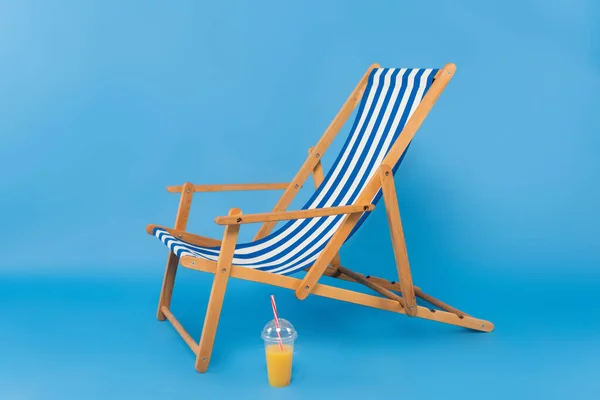 Orange juice near deck chair on blue background — Stock Photo