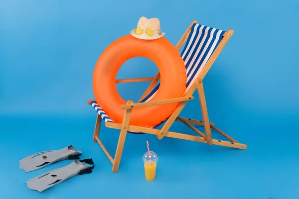 Sombrero de paja en anillo inflable cerca de aletas de natación y jugo de naranja sobre fondo azul - foto de stock