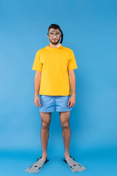 Man in shimming goggles and flippers looking at camera on blue background — Stock Photo