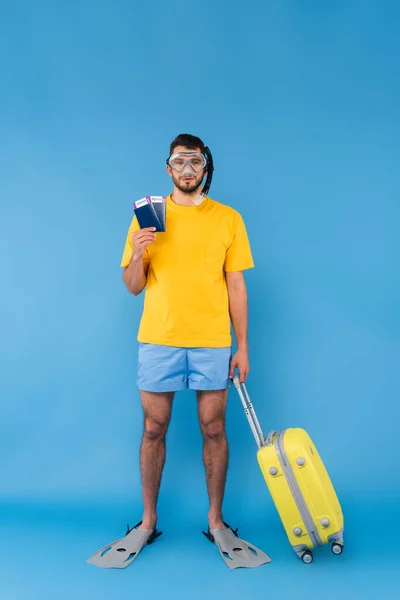 Людина в плавальних лапках і окулярах тримає паспорти і валізу на синьому фоні — стокове фото