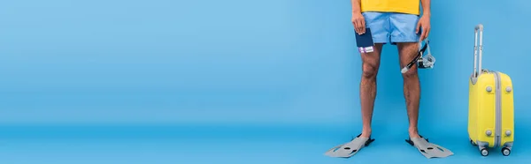 Cropped view of man in swimming flippers holding goggles and passports near suitcase on blue background, banner — Stock Photo