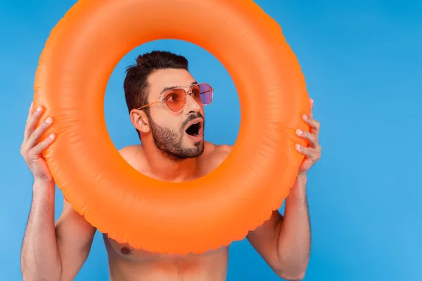 Homme excité dans des lunettes de soleil tenant anneau gonflable isolé sur bleu — Photo de stock