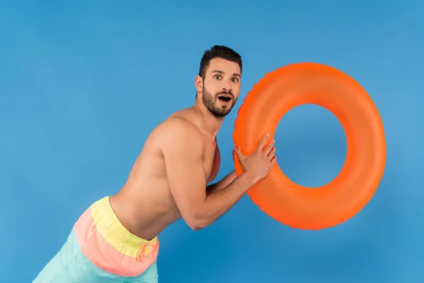 Astonished shirtless man holding inflatable ring isolated on blue — Stock Photo