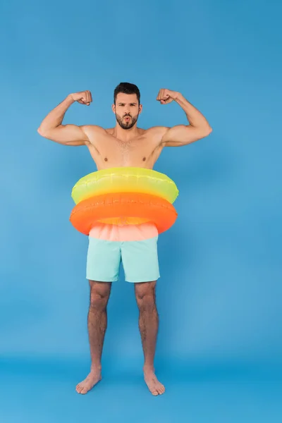 Homem sem camisa em anéis infláveis mostrando músculos no fundo azul — Fotografia de Stock