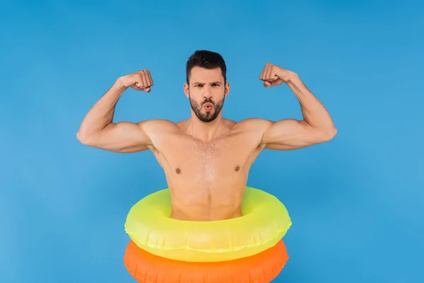 Junger Mann in aufblasbaren Ringen zeigt Muskeln isoliert auf blauem Grund — Stockfoto