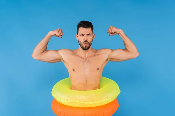 Jovem em anéis infláveis mostrando músculos isolados em azul — Fotografia de Stock