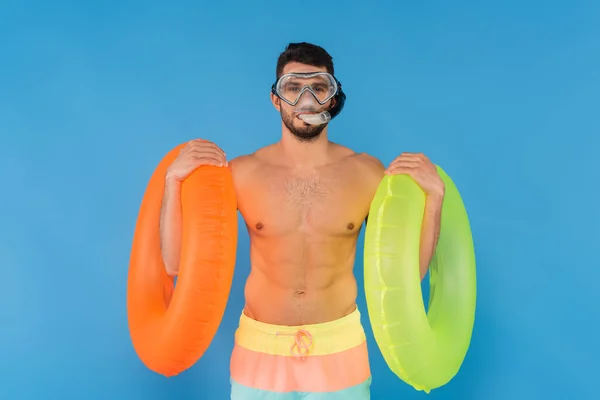 Hombre sin camisa en gafas de natación sosteniendo anillos inflables aislados en azul - foto de stock