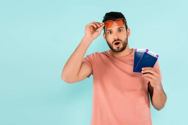 Hombre excitado en gafas de sol con pasaportes y billetes de avión aislados en azul - foto de stock