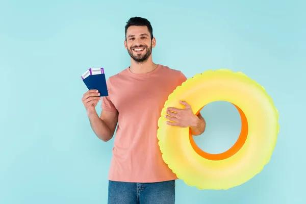 Homem feliz segurando anéis infláveis e passaportes isolados em azul — Fotografia de Stock