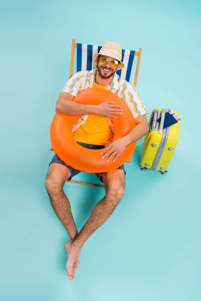 Vista ad alto angolo dell'uomo felice che tiene l'anello gonfiabile vicino alla valigia e ai passaporti su sfondo blu — Foto stock