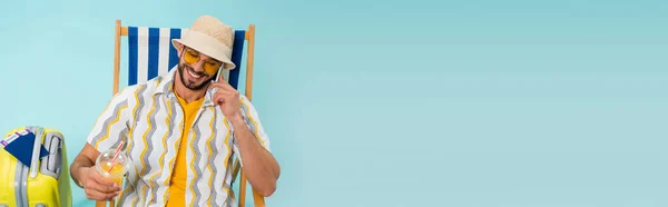 Homme souriant avec du jus d'orange parlant sur téléphone portable près de la valise et passeports sur fond bleu, bannière — Photo de stock