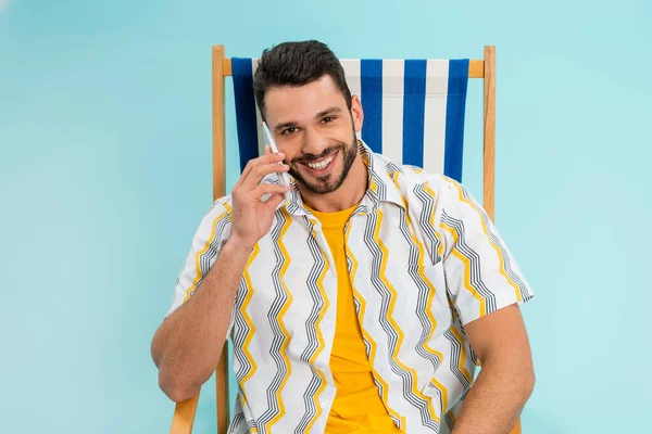Щасливий чоловік говорить на мобільному телефоні на стільці ізольовано на синьому — стокове фото