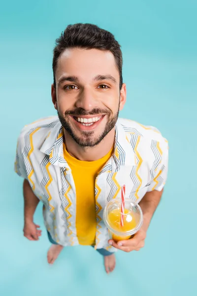 Hochwinkelaufnahme eines positiven Mannes mit Orangensaft auf blauem Hintergrund — Stockfoto