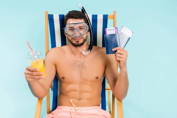 Homme musclé dans des lunettes de natation tenant le jus d'orange et passeports isolés sur bleu — Photo de stock