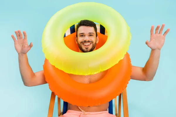 Homem alegre em anéis infláveis que se sentam na cadeira de convés isolada no azul — Fotografia de Stock