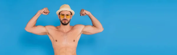 Мужчина без рубашки в солнечной шляпе показывает мышцы на синем фоне, баннер — стоковое фото