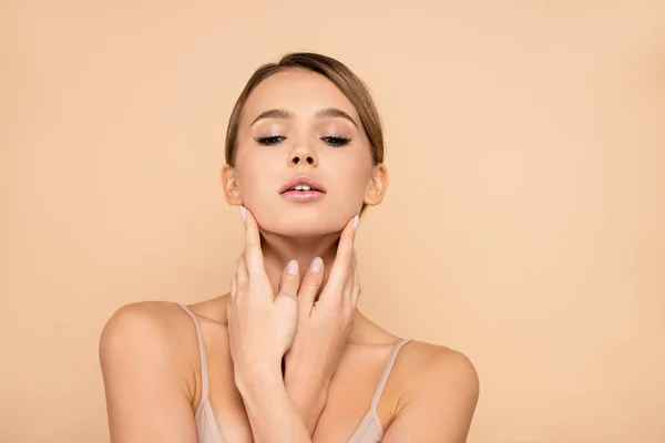 Mujer joven con la piel perfecta cogida de la mano cerca de la cara aislada en beige - foto de stock