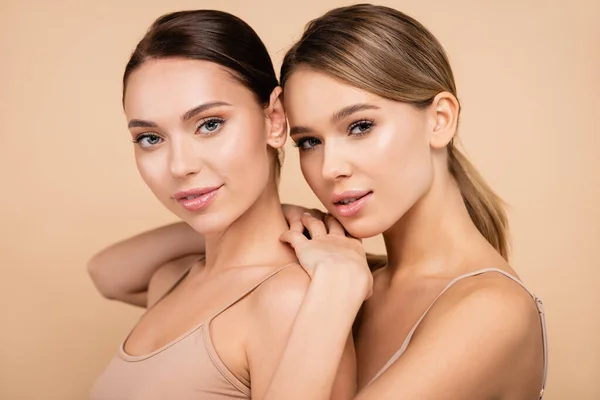 Dos mujeres jóvenes con maquillaje natural posando aisladas en beige - foto de stock