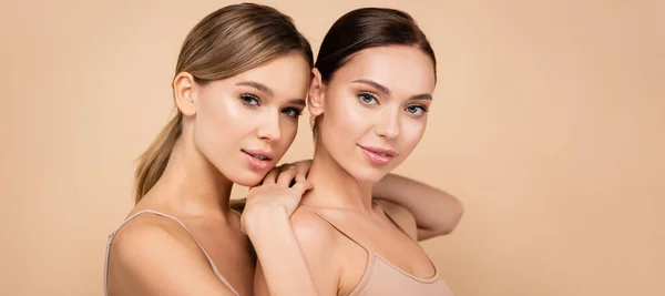 Young woman with perfect skin leaning on shoulder of pretty friend isolated on beige, banner — Stock Photo